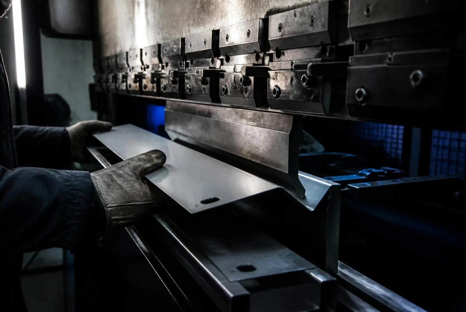 Prensa dobladora CNC formando una lámina de acero, operador con guantes de protección